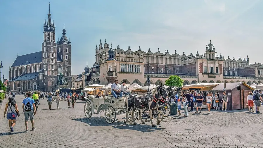 Blick auf den MArktplatz von Krakau. Im Vordergrund fährt eine Kutsche über den Platz, im Hintergrund ist die Marienkirche zu sehen.